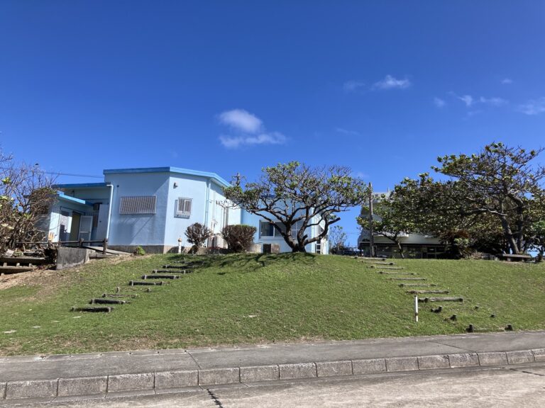 青空の下に建つ建物と緑の庭